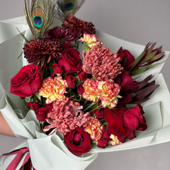 Bouquet of red and pink flowers with peacock feathers on a gray background