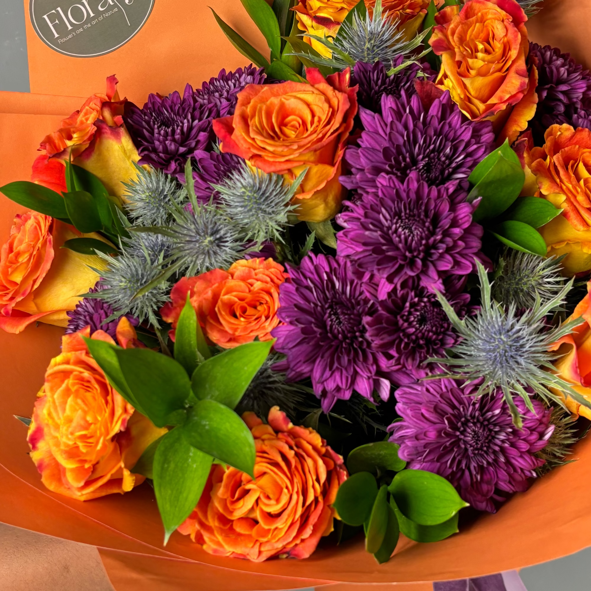 Bouquet of orange and purple flowers with an orange wrap, featuring the 'Floraty' brand.