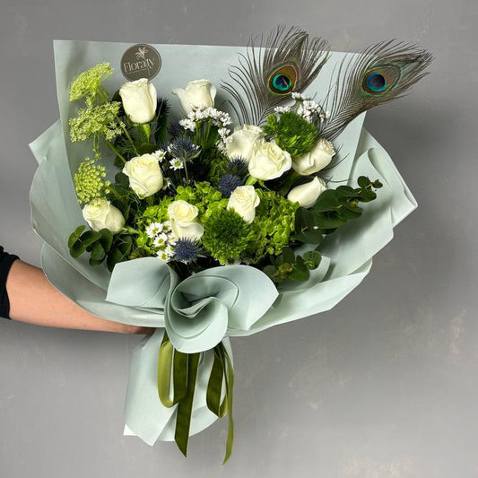 Bouquet of flowers with peacock feathers held by a person against a gray background