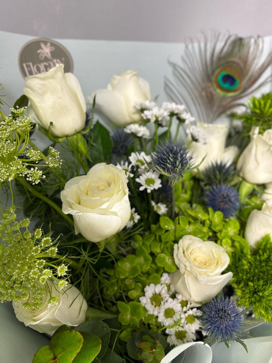Bouquet of white roses with greenery and a peacock feather on a gray background

