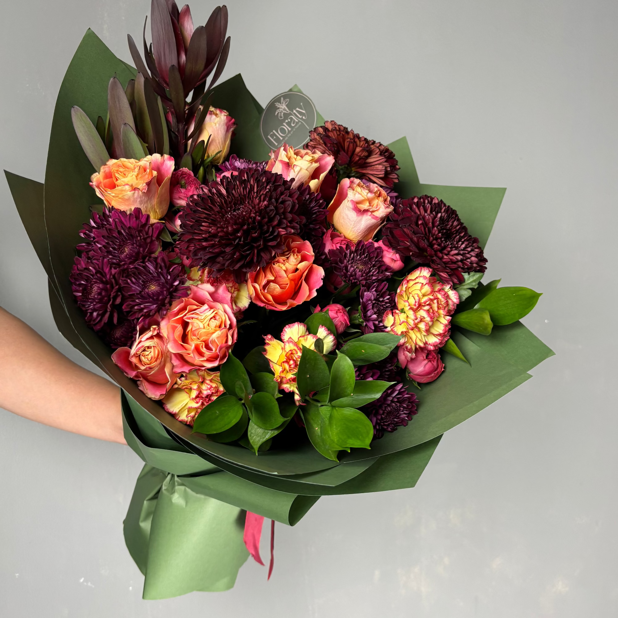 Bouquet of flowers with dark red and orange flowers held by a person against a light gray background