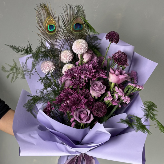Bouquet of flowers with peacock feathers wrapped in purple paper on a light gray background