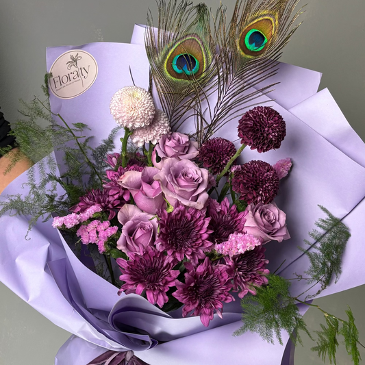 Bouquet of flowers with peacock feathers and a visible brand label on a light gray background