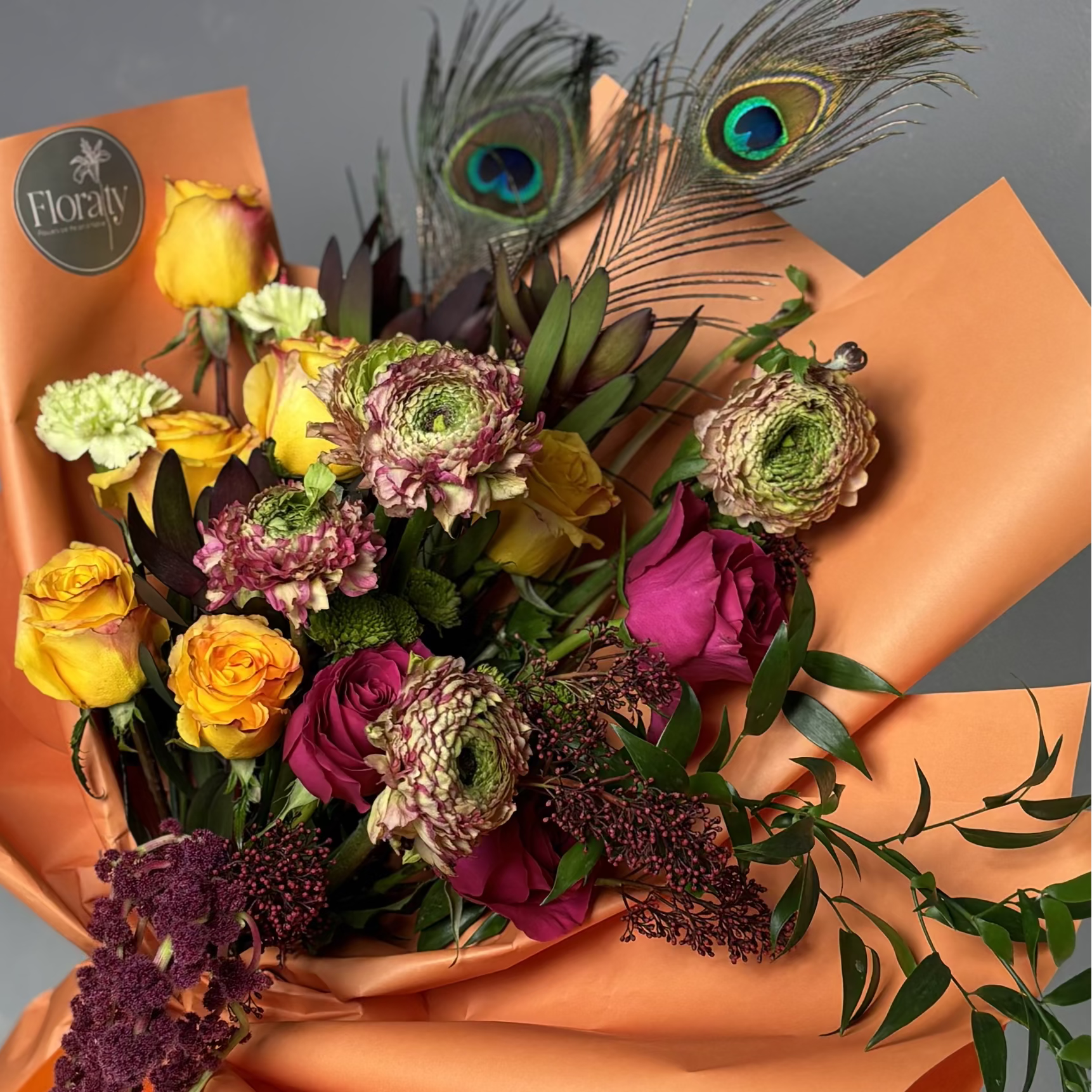 Bouquet of flowers with peacock feathers on orange paper, brand 'Floraty' visible