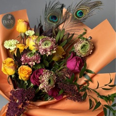 Bouquet of flowers with peacock feathers on orange paper, brand 'Floraty' visible