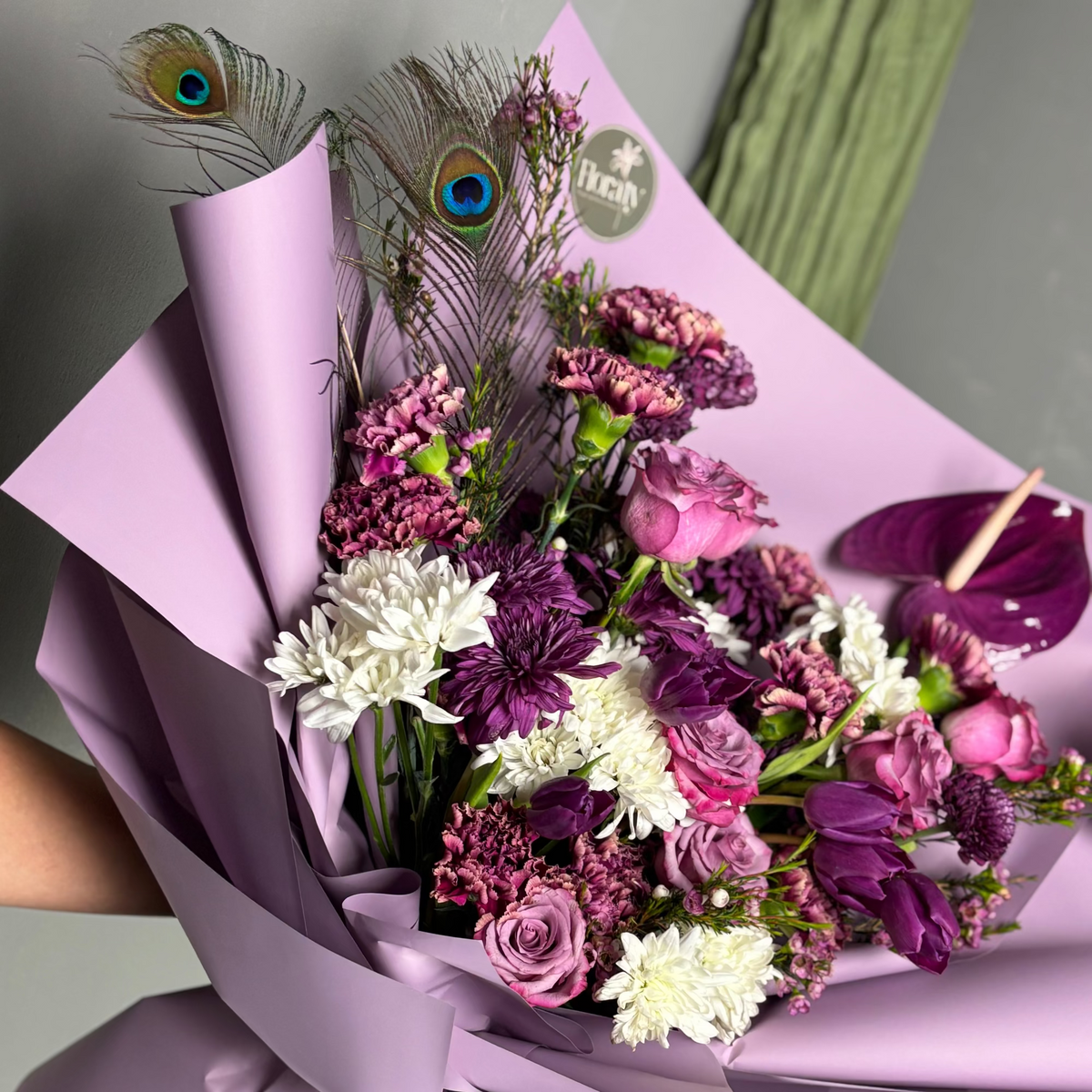 Bouquet of flowers with purple and white colors, wrapped in pink paper, held by a person.