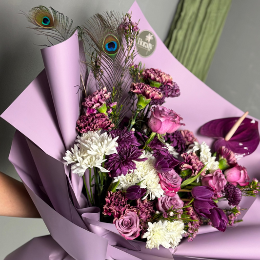 Bouquet of flowers with purple and white colors, wrapped in pink paper, held by a person.