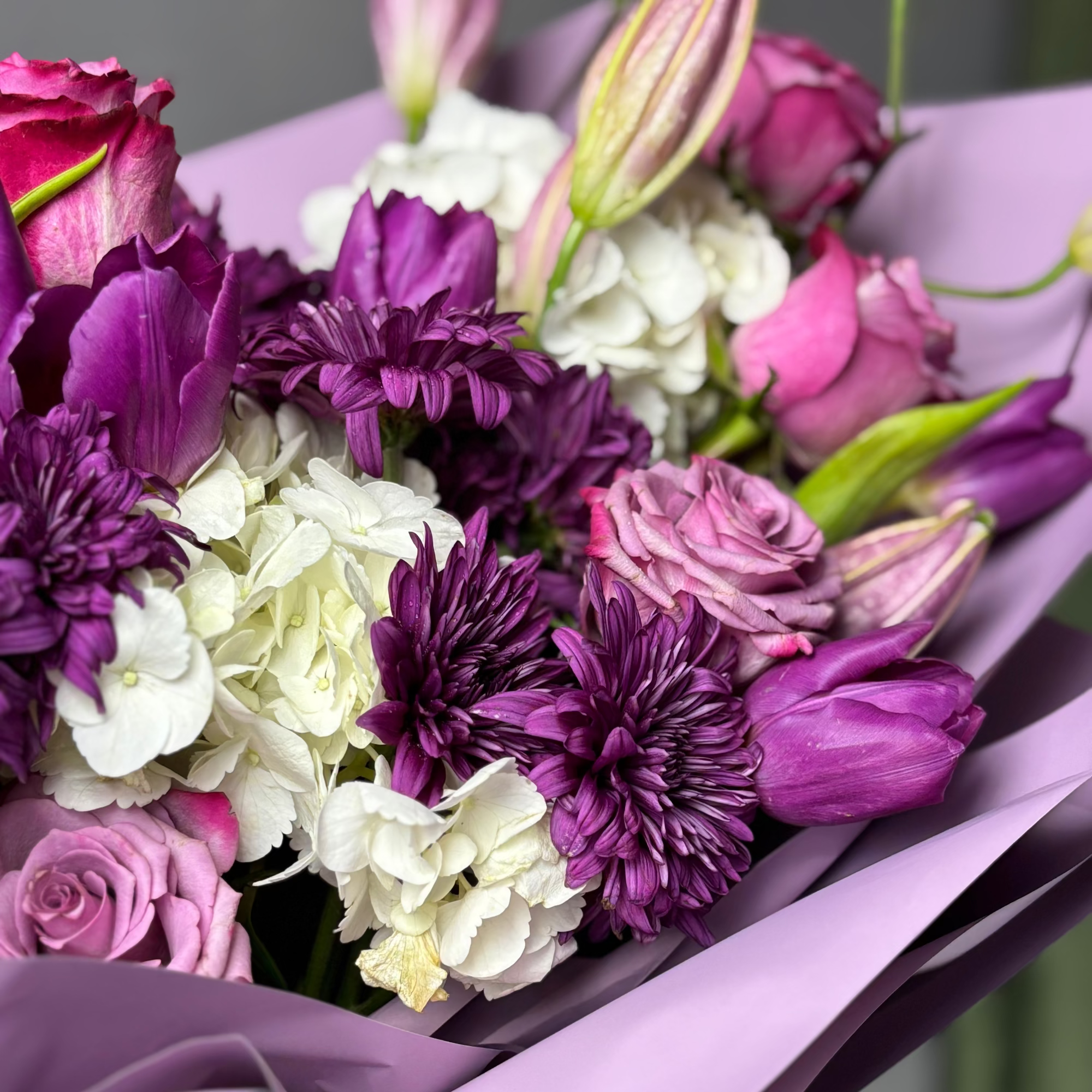 Bouquet of purple, white, and pink flowers with a purple ribbon on a blurred background