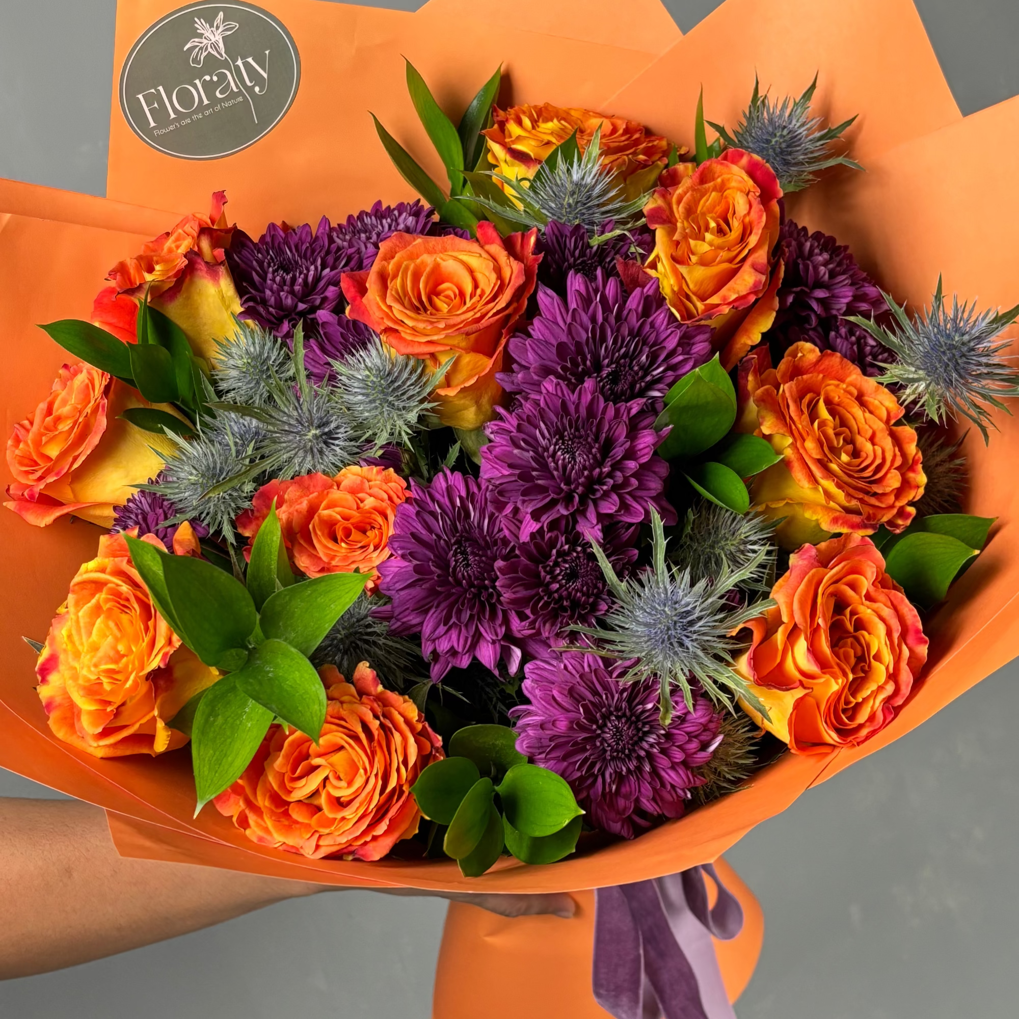 Bouquet of orange and purple flowers with a visible 'Floraly' logo on orange paper.

