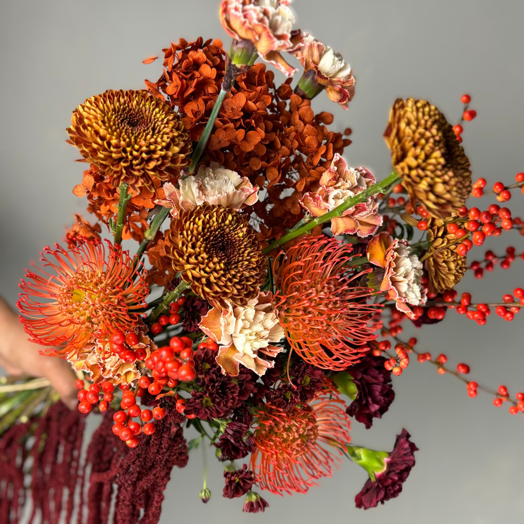 Bouquet of autumnal flowers with oranges, reds, and browns on a neutral background