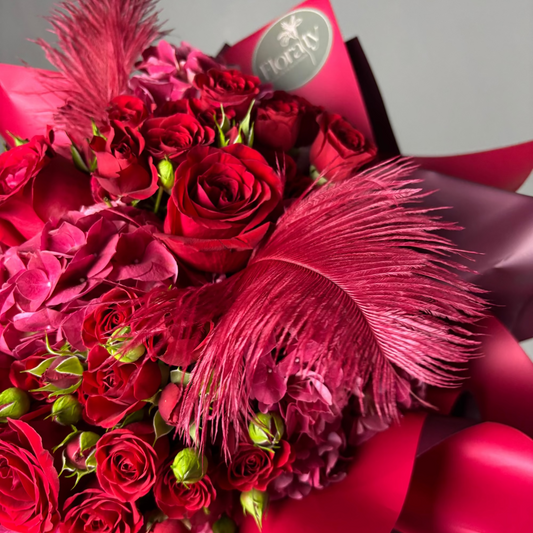Bouquet of red roses with pink feathers and a visible brand logo on a gray background
