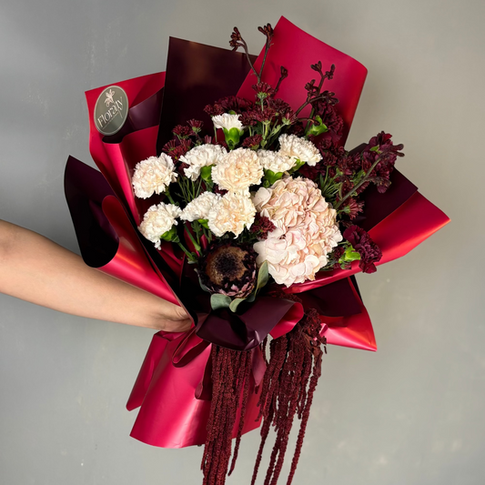 Bouquet of flowers wrapped in red paper held by a person against a gray background

