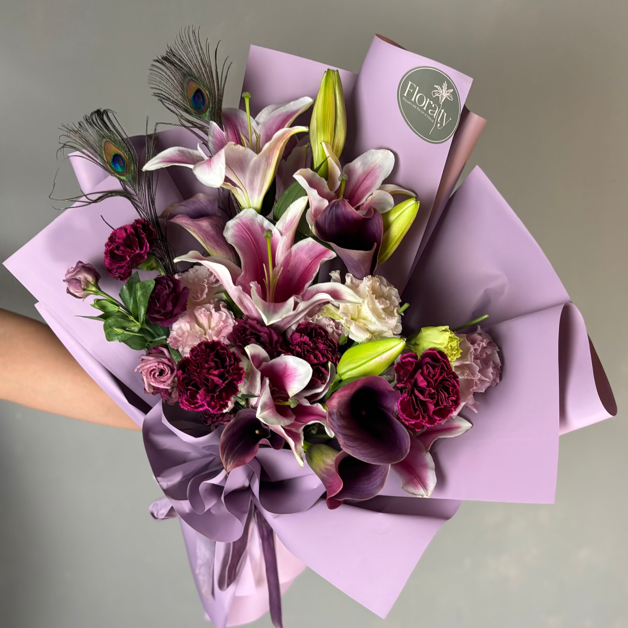 Bouquet of flowers wrapped in purple paper with a visible brand logo on a gray background