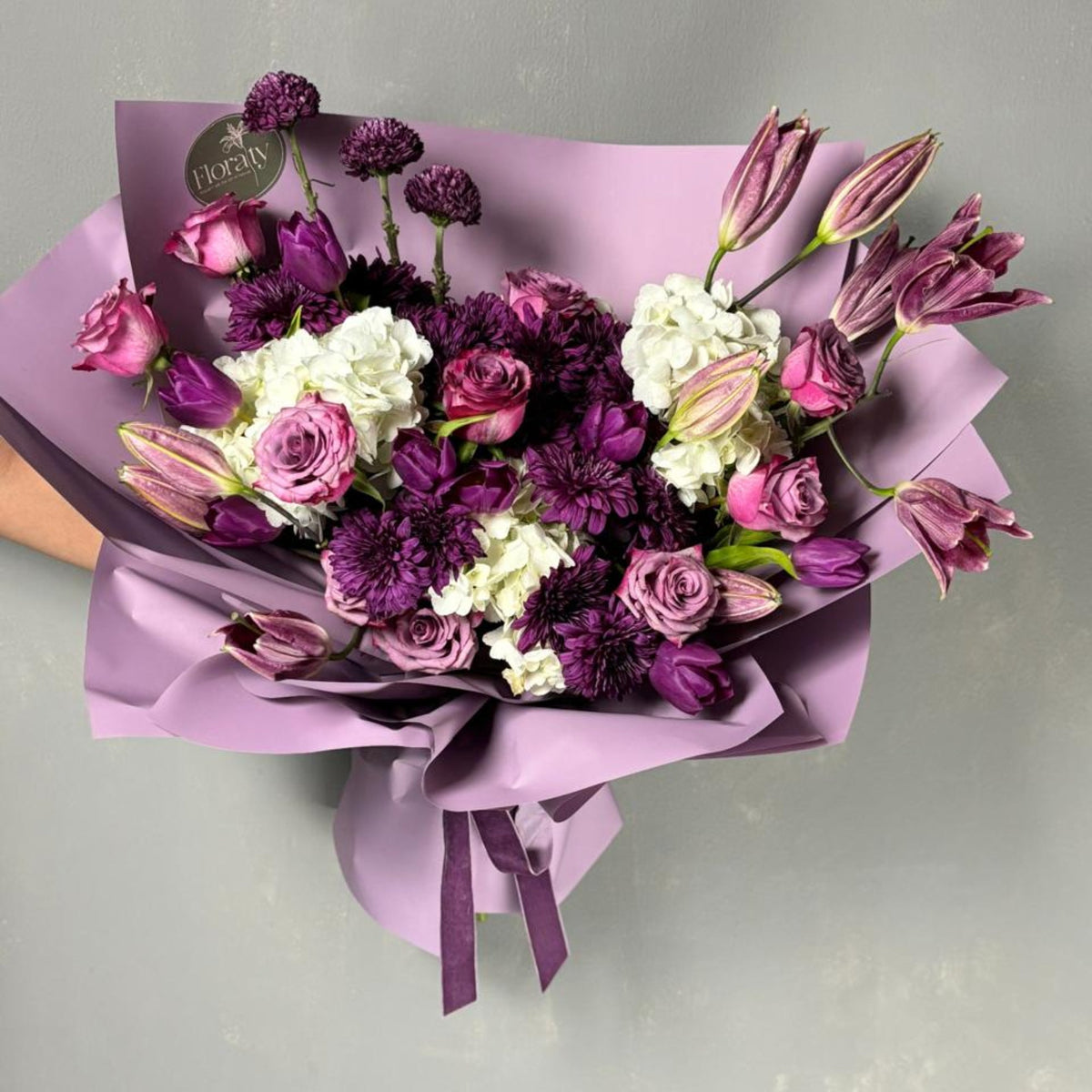 Bouquet of purple and white flowers wrapped in purple paper on a light gray background